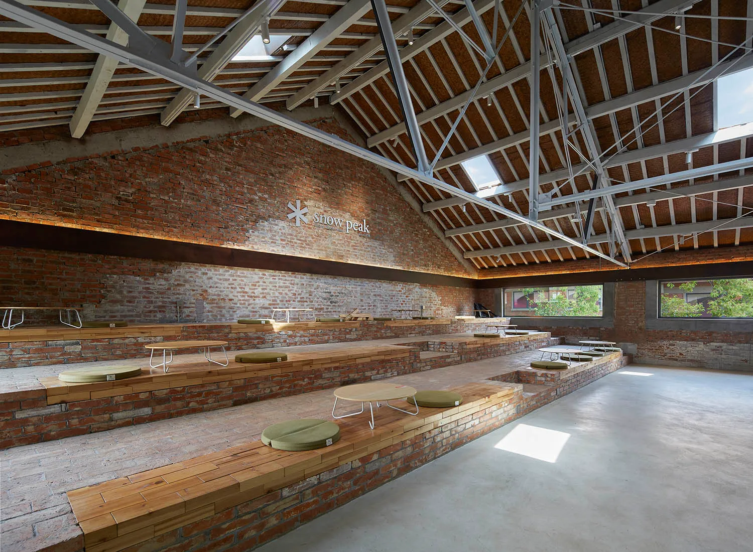 A large brick building with a high ceiling, featuring a dining area with multiple tables and chairs, and several benches for social gatherings or events