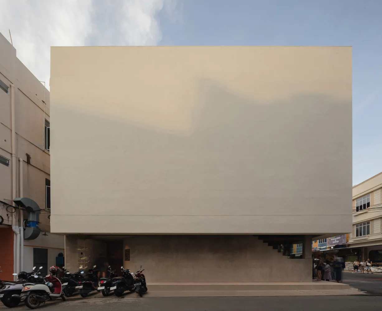 A modern building with a blank white wall, surrounded by motorcycles and people standing around the area
