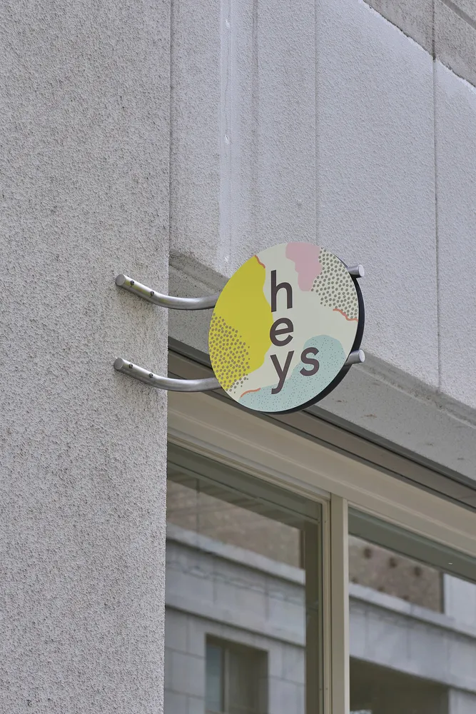 A concrete building exterior with a yellow sign featuring white letters that spell out Hey's