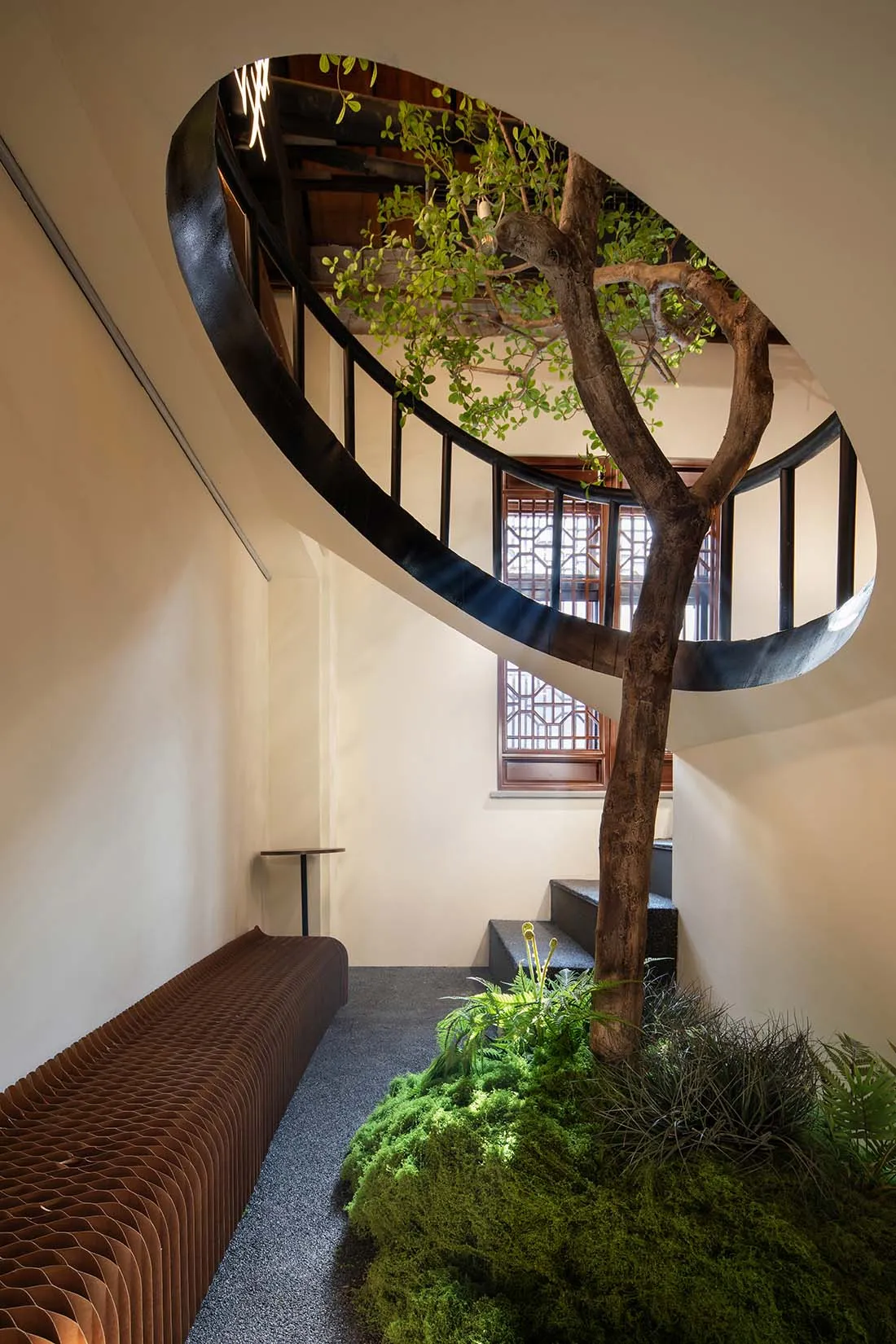 A modern spiral staircase with a wooden structure and black railing, set in a well-lit living area with a bench at the base