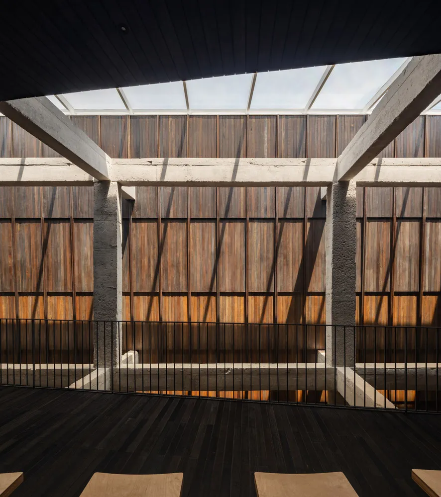A large building with wooden walls and floors, featuring multiple rooms and hallways, with a warm and rustic atmosphere, and chairs placed within the space