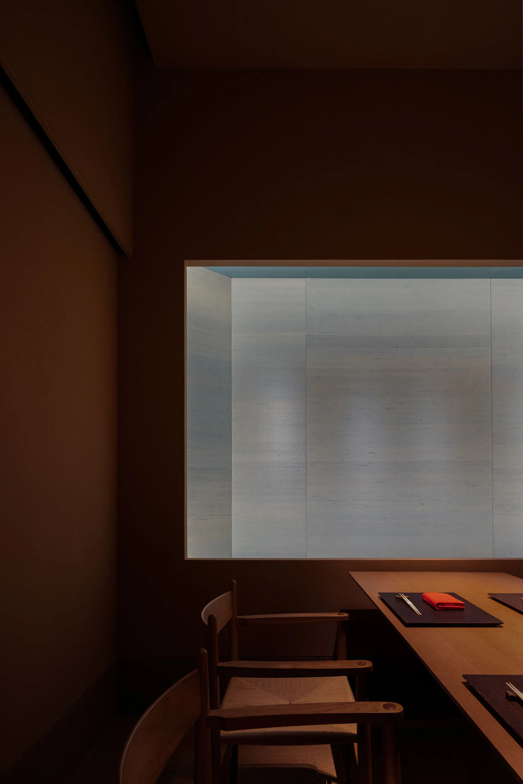 Dimly lit room with a glass wall, two chairs, a dining table, and a book, in a modern and minimalist style