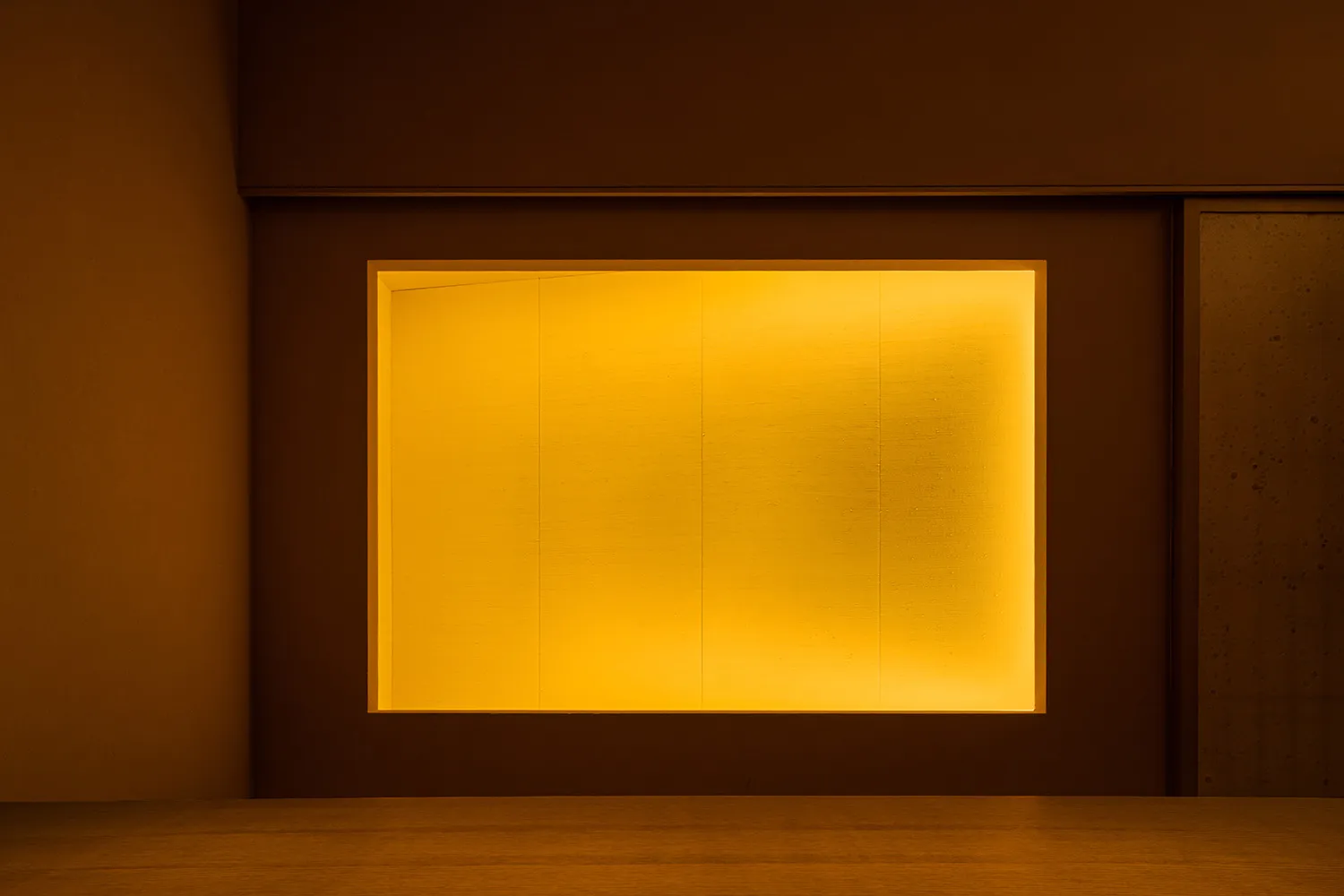 A large, open room with a yellow wall, wooden texture, and natural light from a window