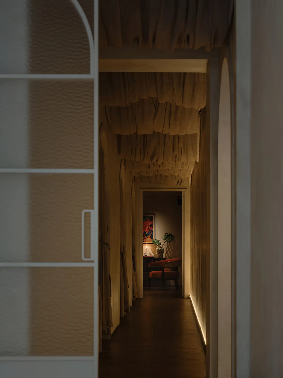 A carpeted hallway leads to a bedroom with two chairs and a potted plant, creating a cozy atmosphere