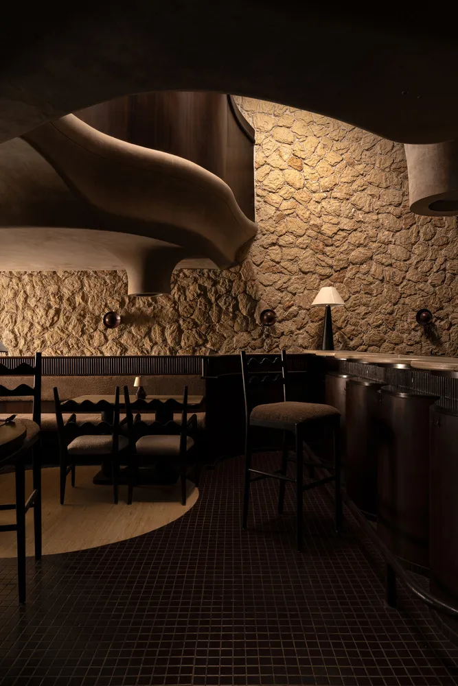 Cozy restaurant interior with a curved ceiling, stone walls, and dining tables, chairs, and bottles