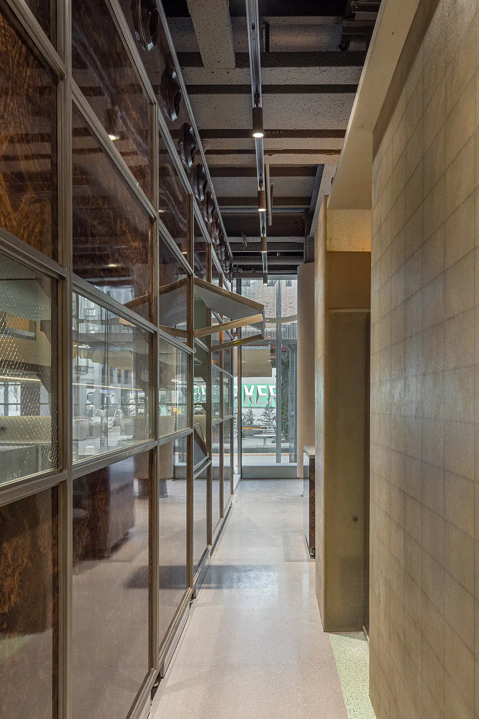 A well-lit restaurant hallway with glass walls, a wooden floor, and chairs for seating