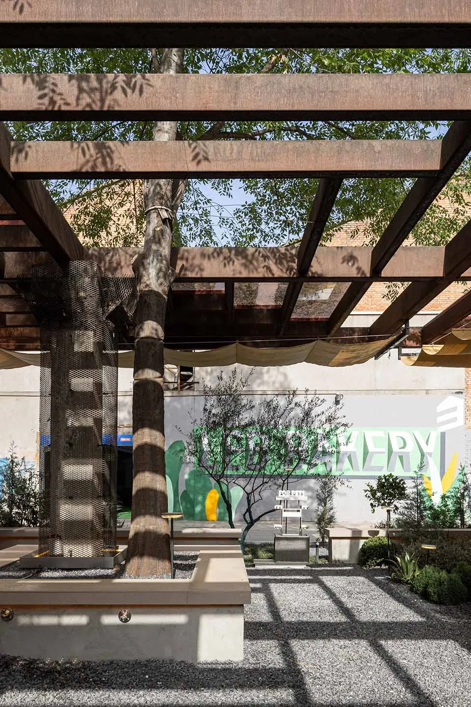 A spacious interior space with a large tree in the center, surrounded by chairs and a dining table, with a focus on nature and relaxation