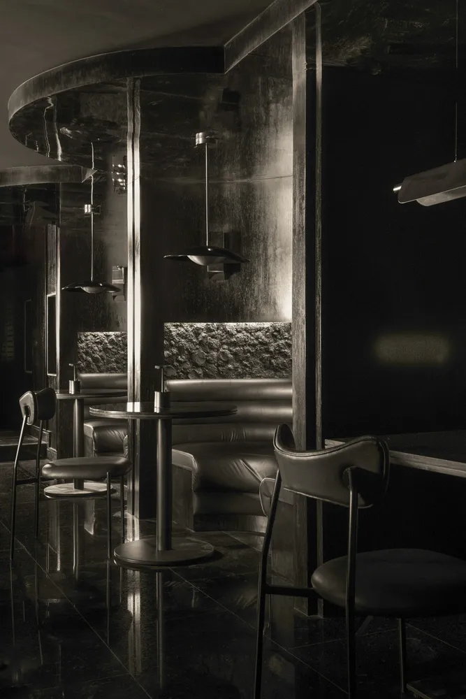 Elegant restaurant interior with multiple dining tables, chairs, a bar, and couches, featuring a black and white color scheme