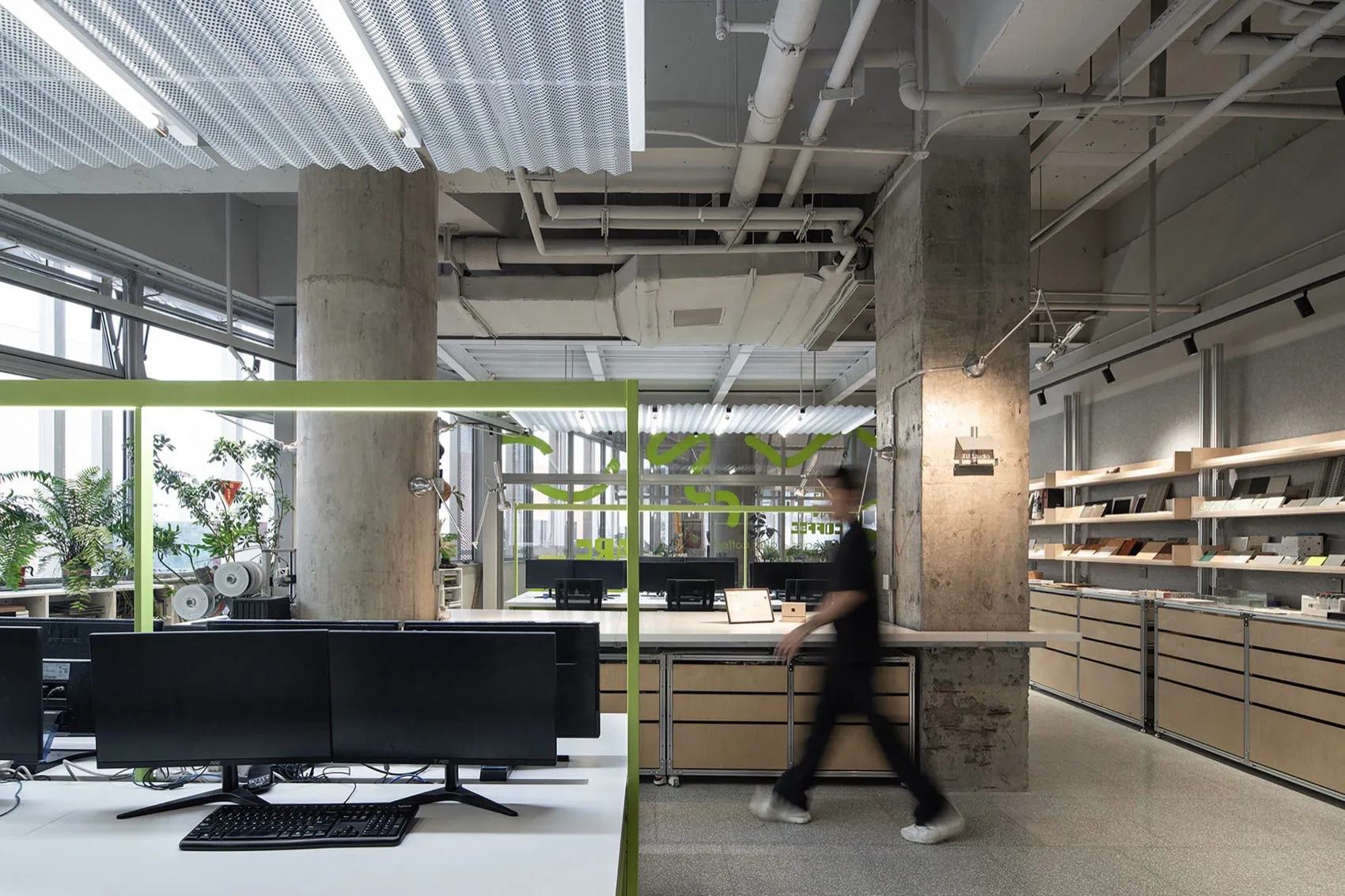 A professional office space with modern furniture, multiple TV screens, and a person walking through the room, conveying a sense of functionality and organization