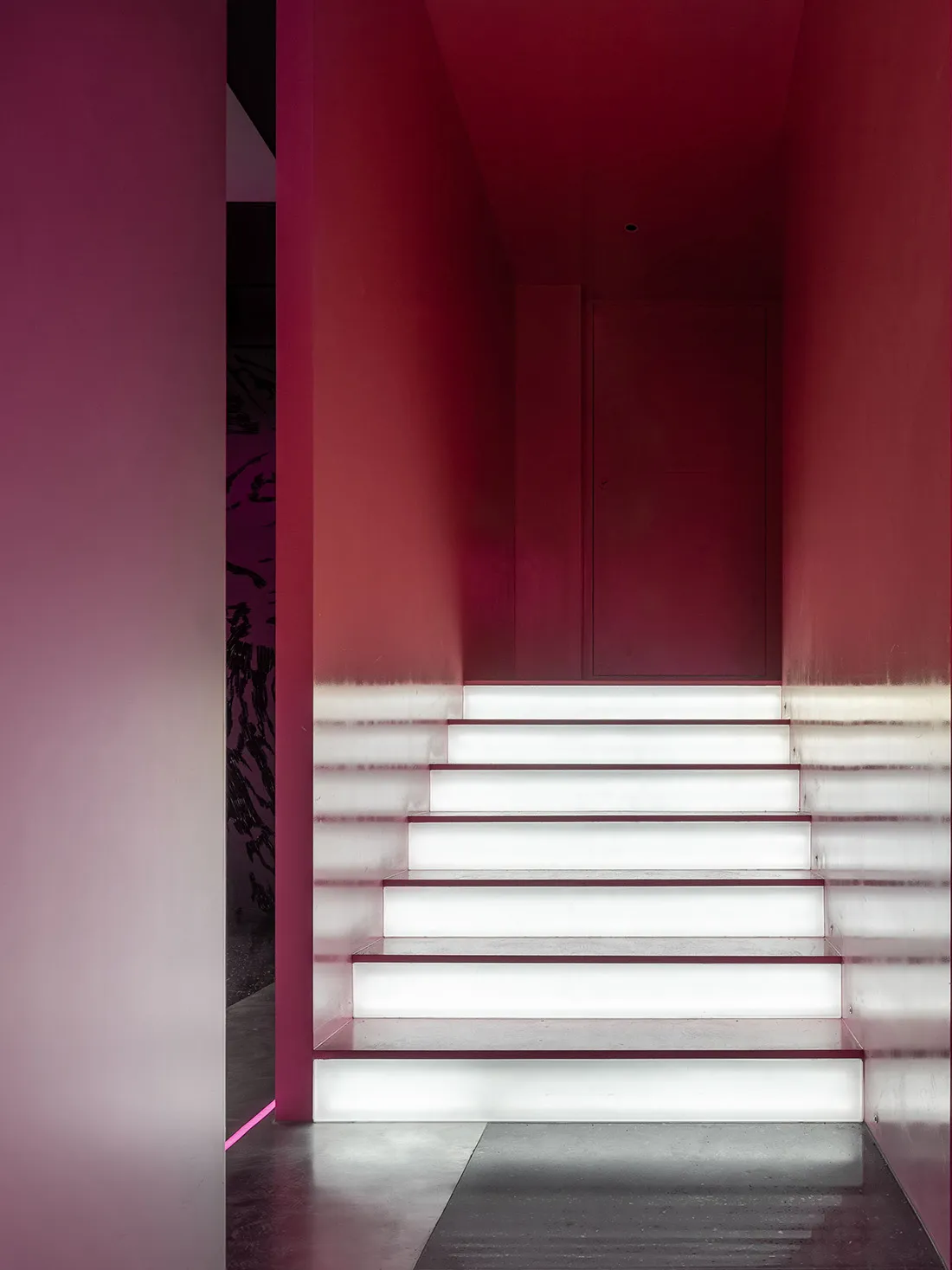 A grand staircase in a museum setting with marble steps, a red wall, and a sense of elegance