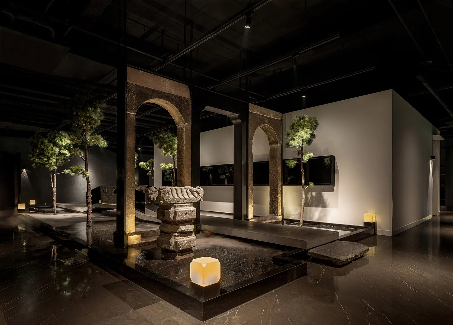 A calm and inviting art gallery space featuring a large stone sculpture, potted plants, and two vases, with a focus on the impressive stone centerpiece
