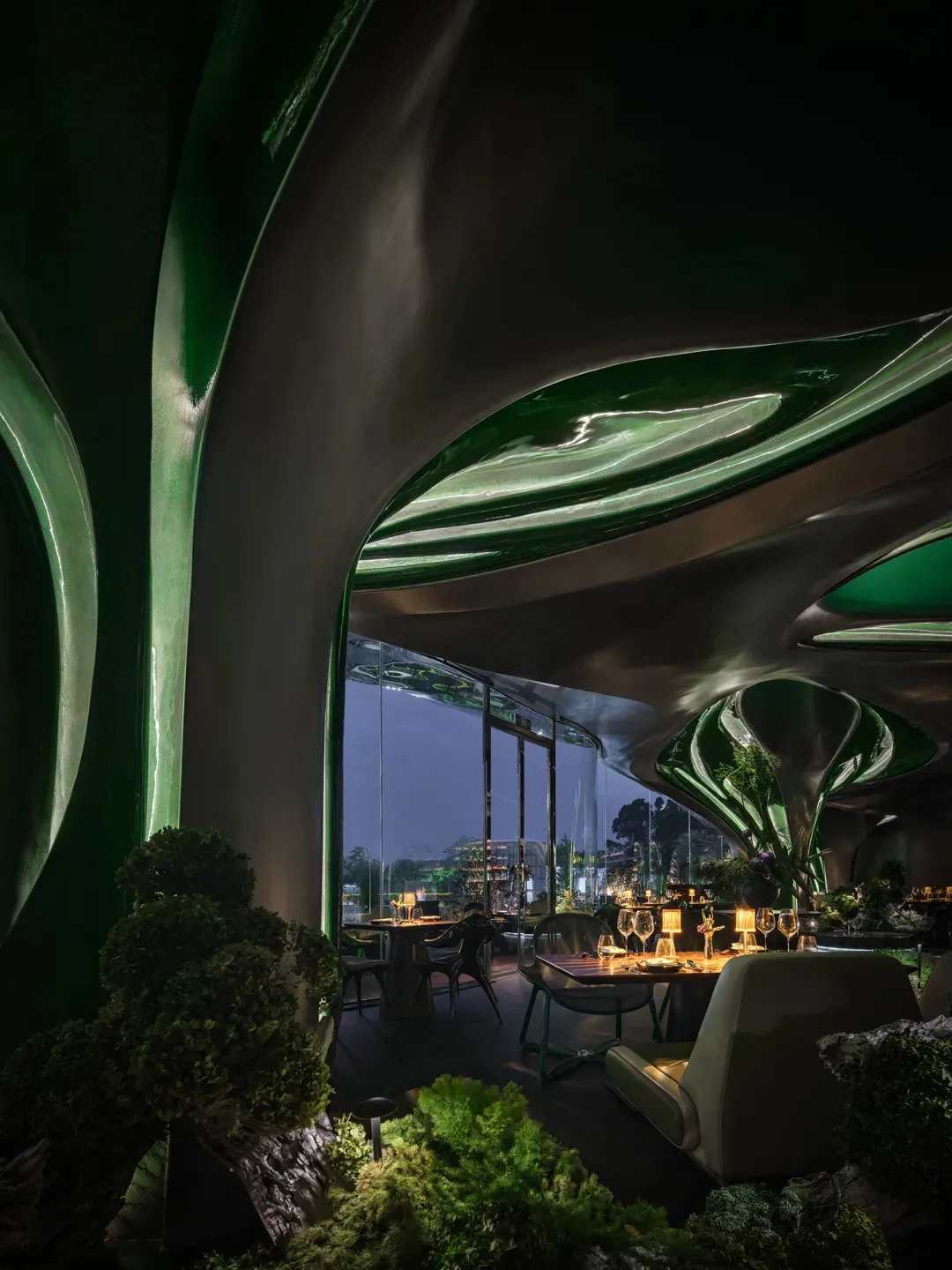 A cozy restaurant dining area with a large green wall, multiple chairs, and dining tables with wine glasses and bottles