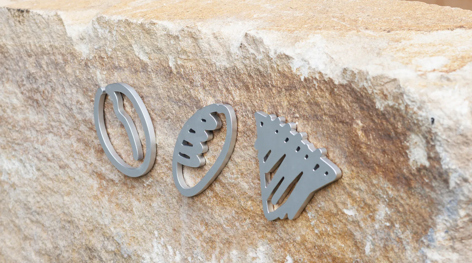 Three metal sculptures resembling footballs, pizza slices, and a house are arranged on a rock surface, showcasing creativity and craftsmanship
