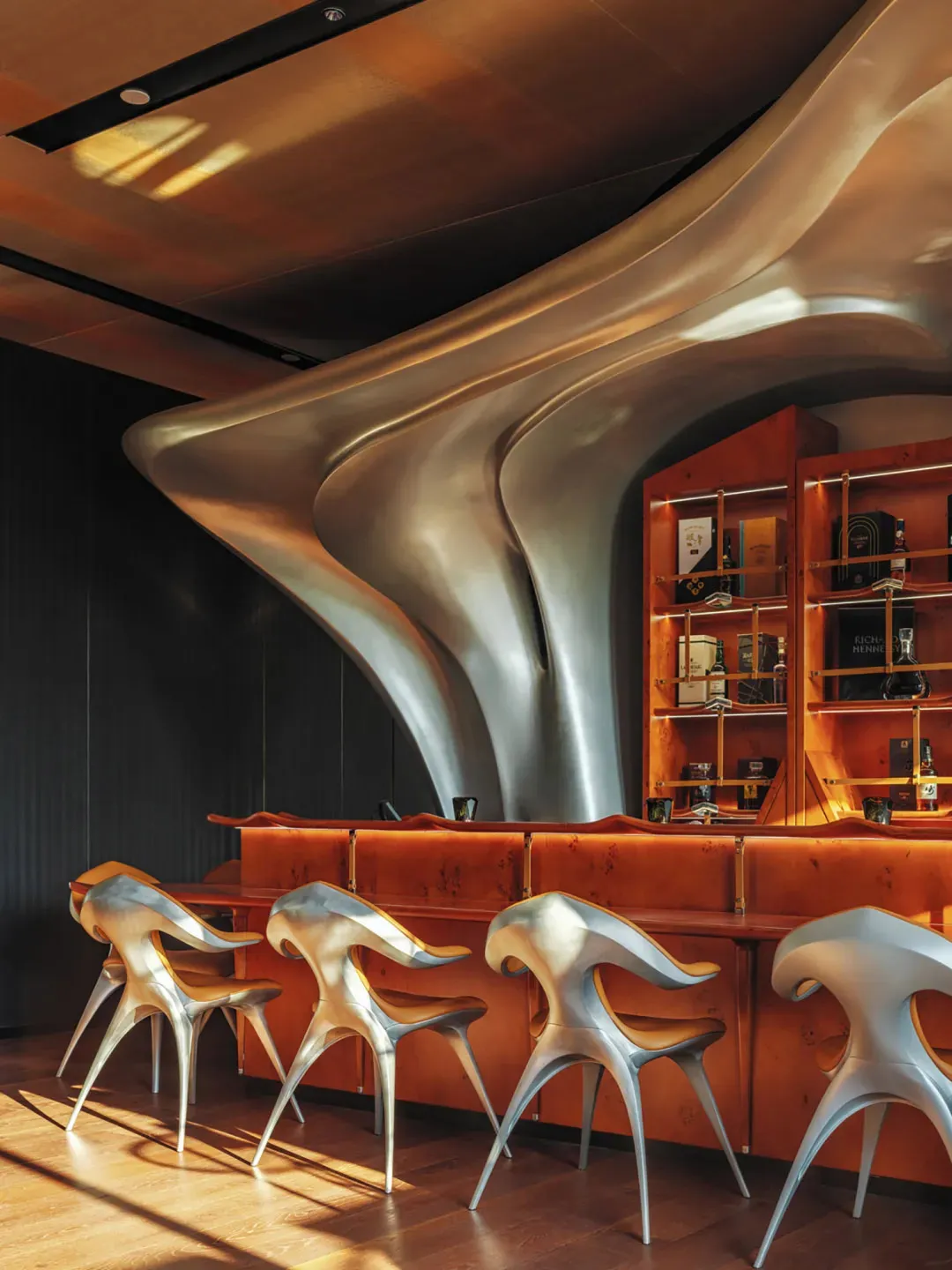 A modern bar area with a curved wall, four chairs, and a counter, creating an inviting atmosphere for socializing and enjoying drinks