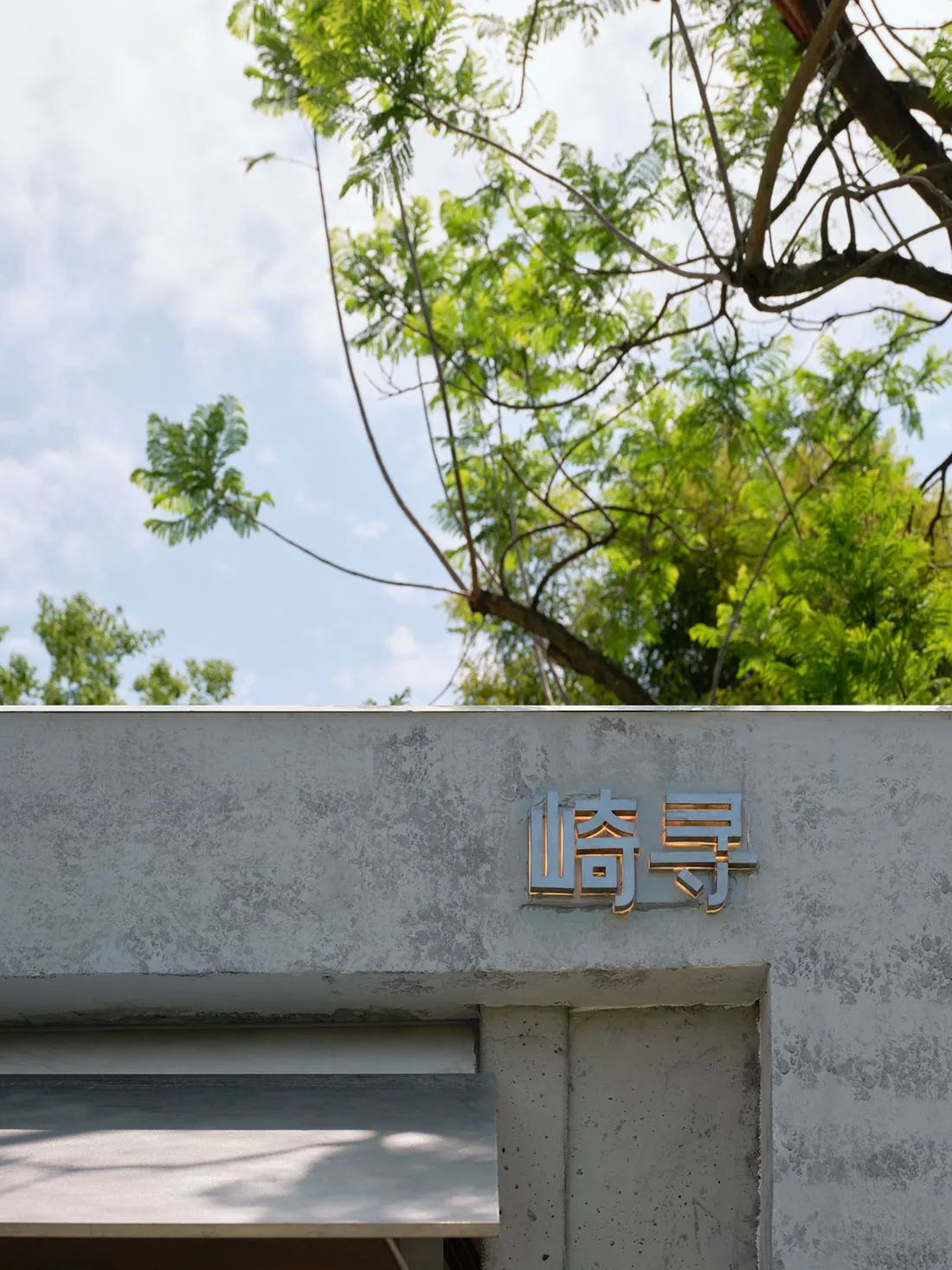 灰色混凝土建築，帶有金屬招牌與現代外觀，周圍環繞樹木，位於都市環境中