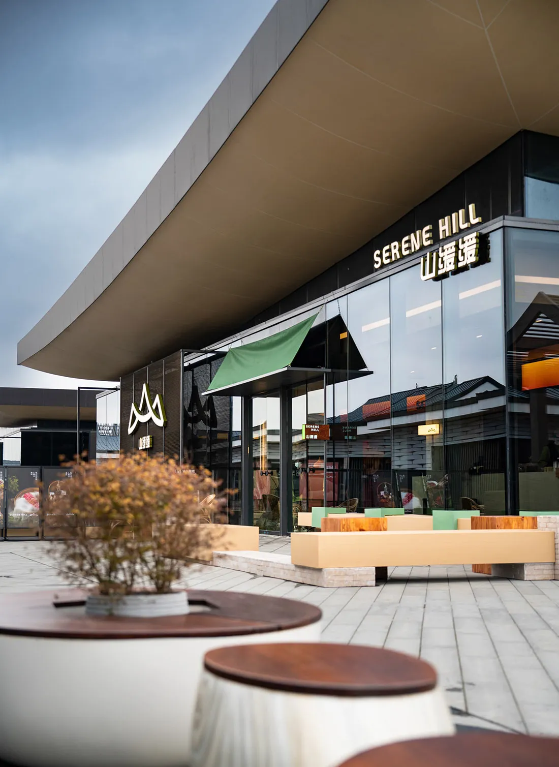 A modern shopping center with a glass building, chairs, and dining tables, creating an inviting and comfortable atmosphere for visitors