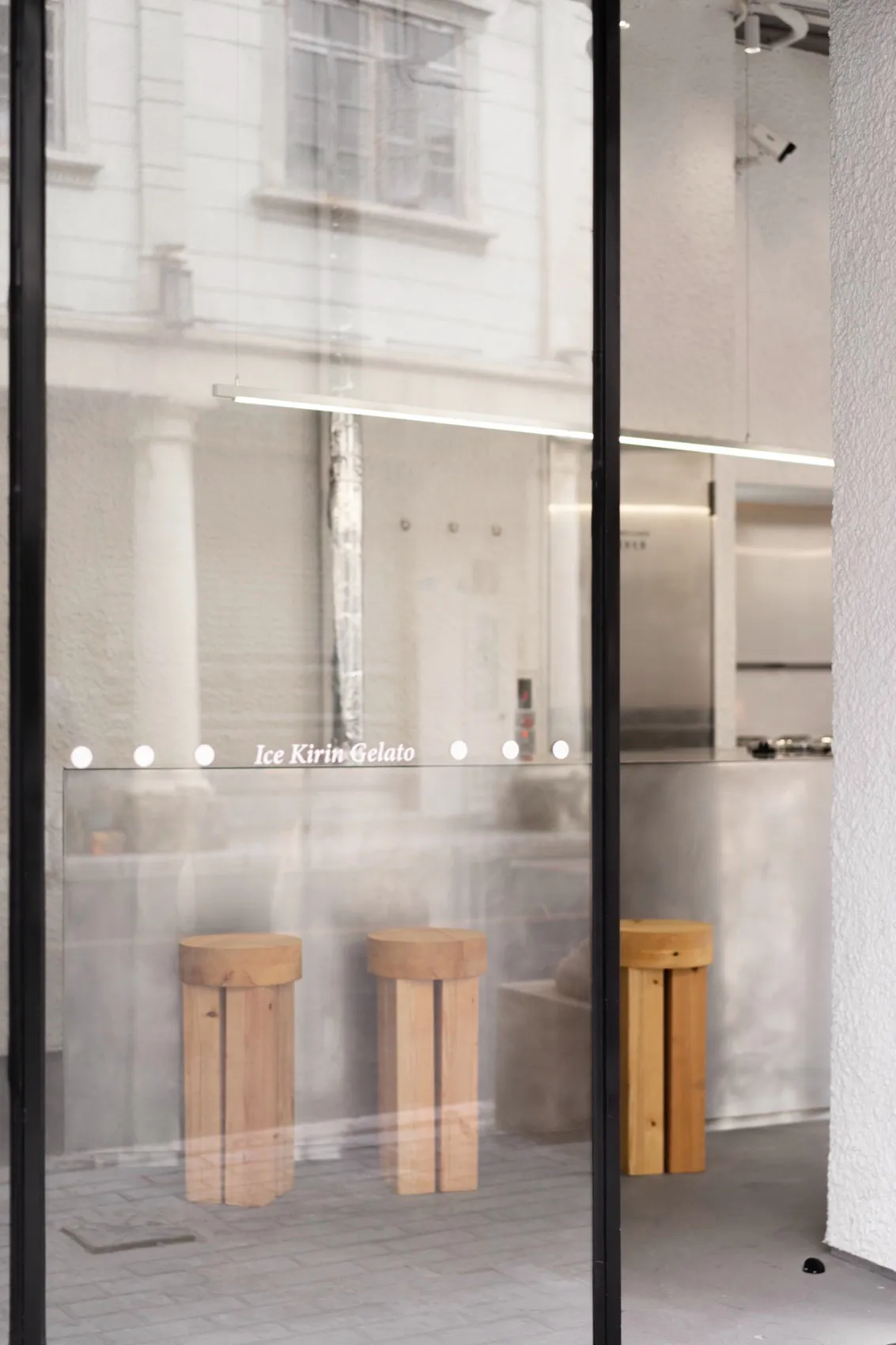 An inviting ice cream shop with wooden stools, a display case, and a refrigerator, set against a neutral background