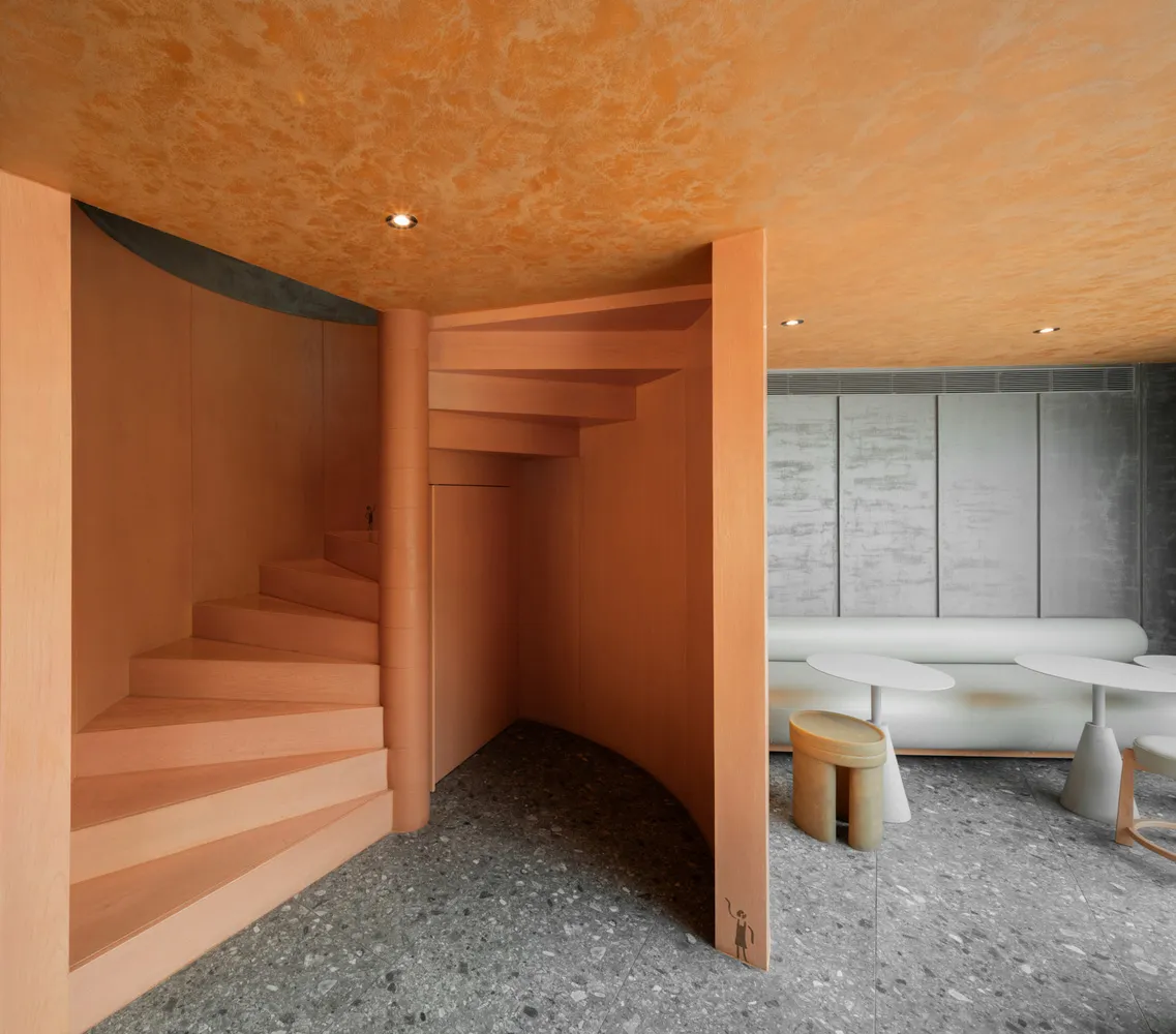 A modern living space with a spiral wooden staircase, orange walls, and a cozy bench at the base of the stairs