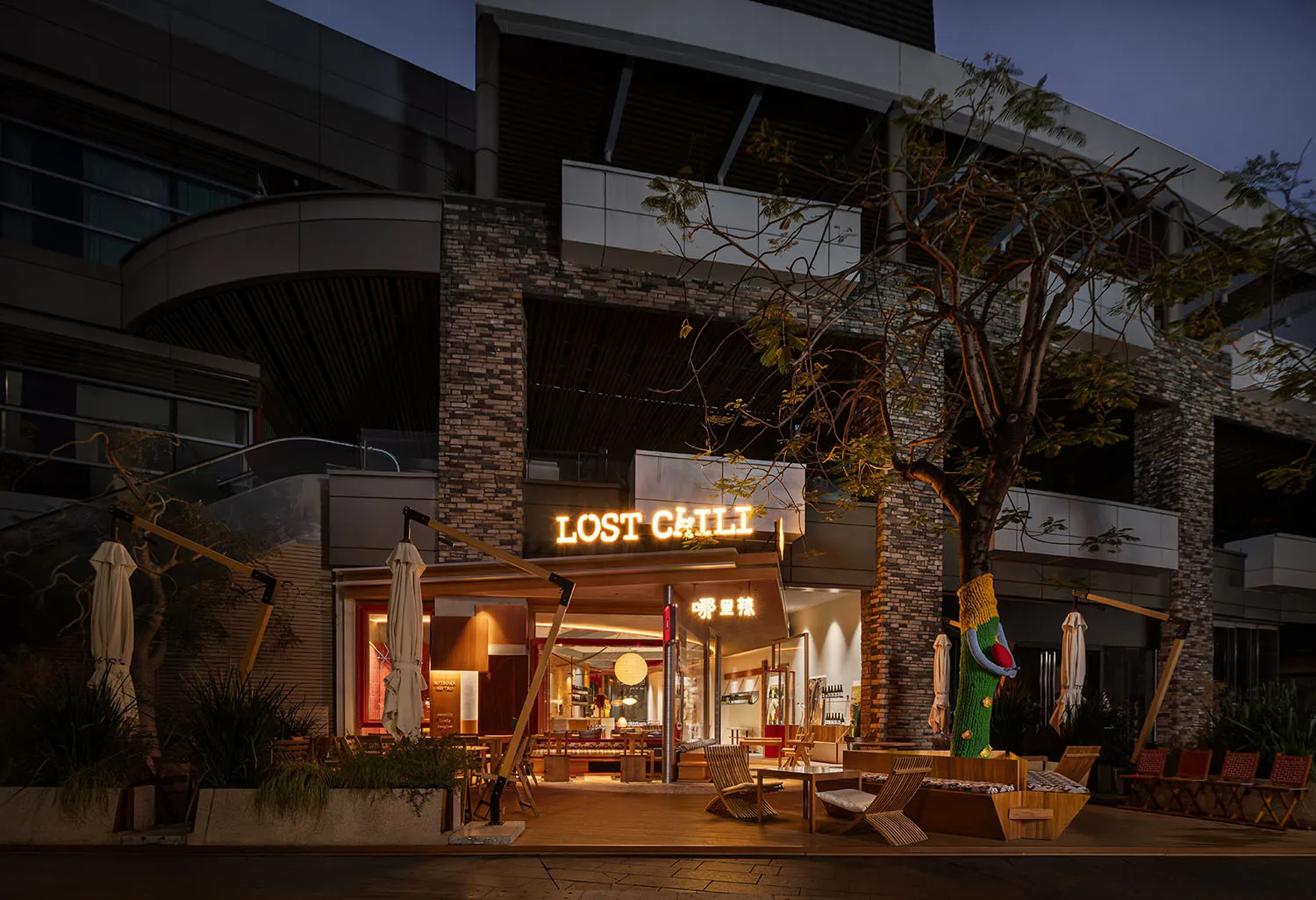 Cozy outdoor dining space with tables, chairs, umbrellas, and a mix of wood and metal materials under warm lighting