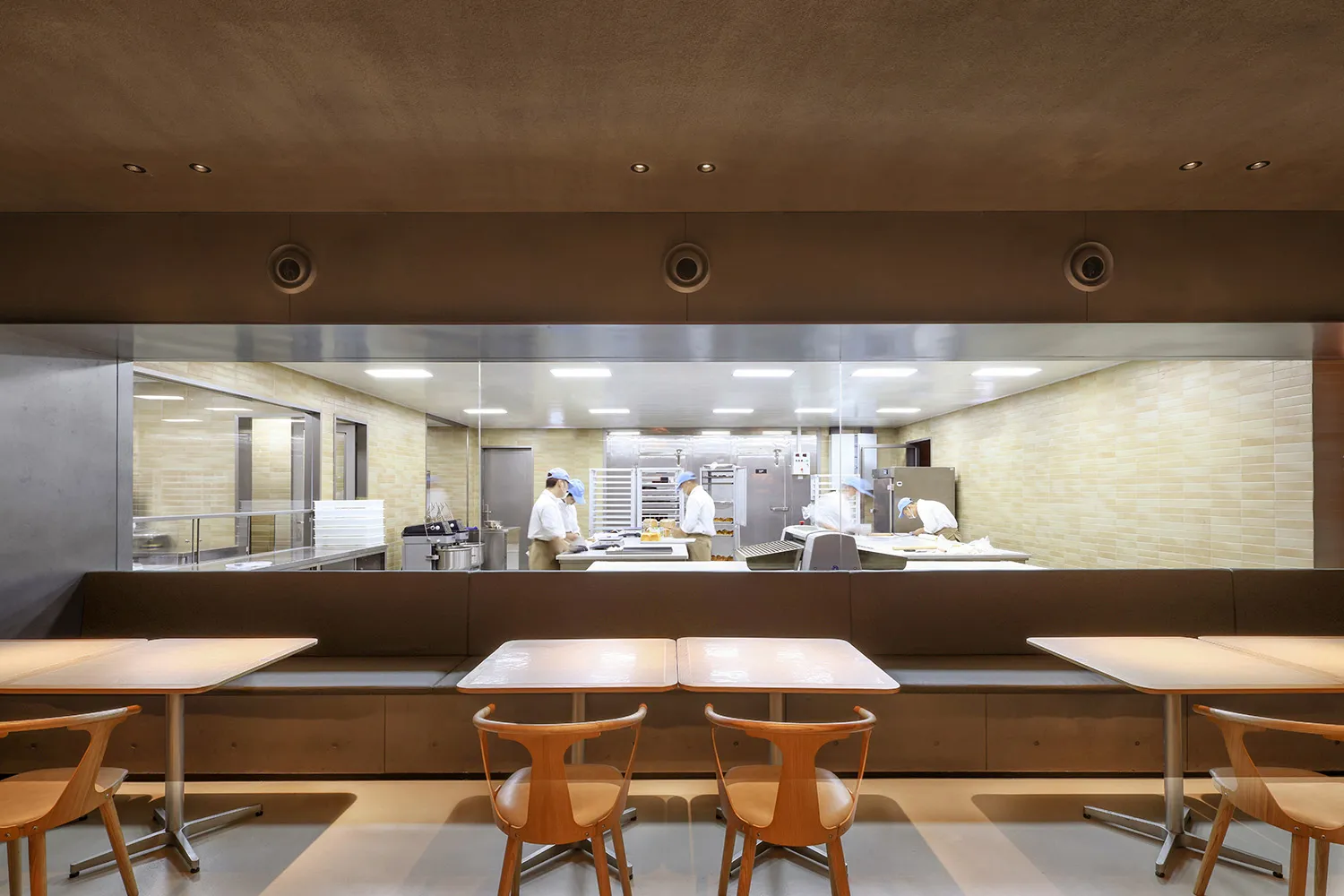 Industrial kitchen dining area with wooden tables, chairs, appliances, and natural light from a window