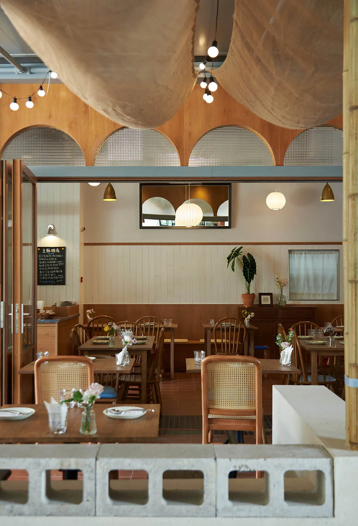 Warm restaurant interior with wooden tables, chairs, and flooring, surrounded by potted plants and a blend of traditional and modern elements