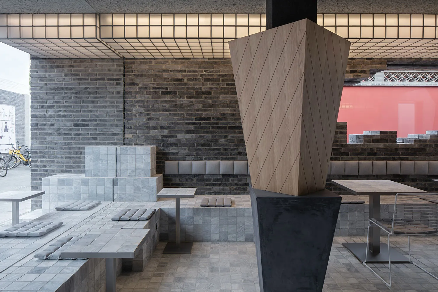 A modern restaurant interior with a large wooden sculpture, grey stone walls, and a black and white theme, featuring tables and chairs in a stylish and inviting atmosphere