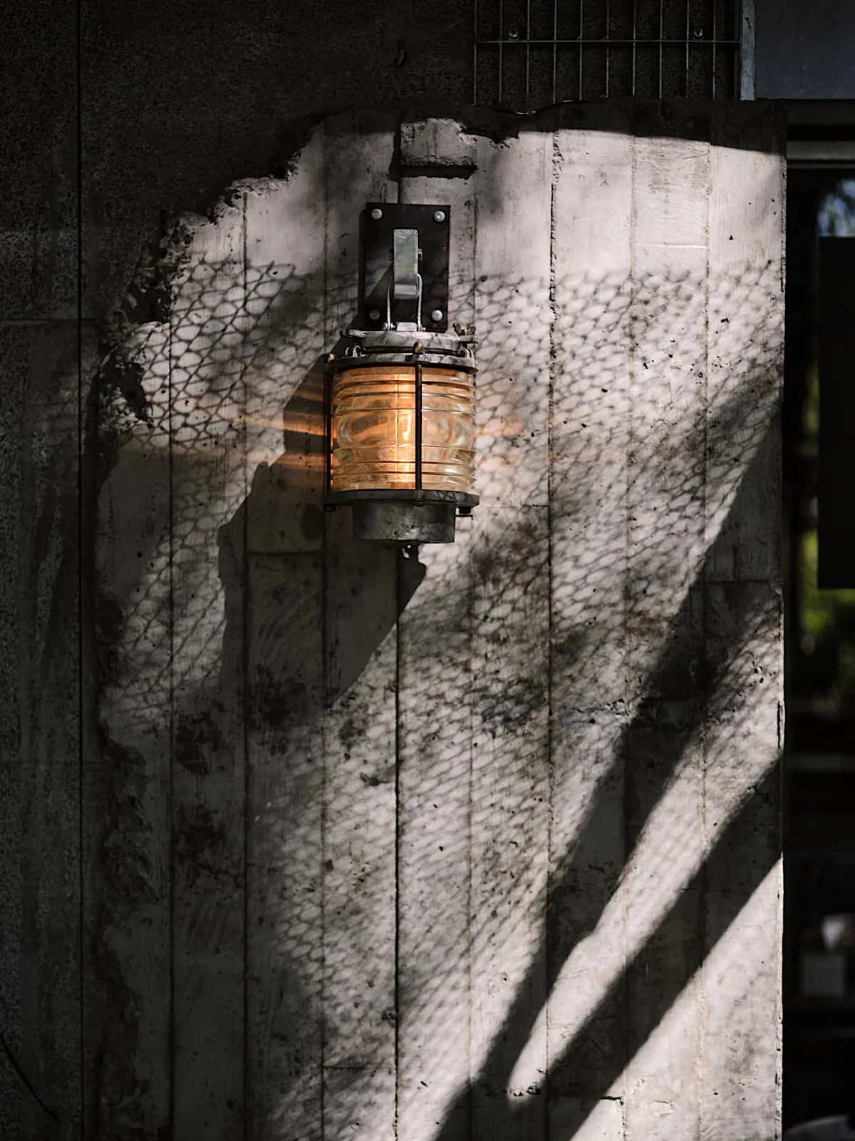 Old building with a stone wall featuring a metal lamp and a light fixture, suggesting a historical setting