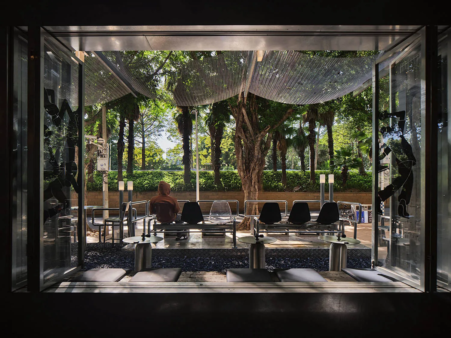 Outdoor seating area with various chairs and tables on a cement surface, surrounded by trees and natural light