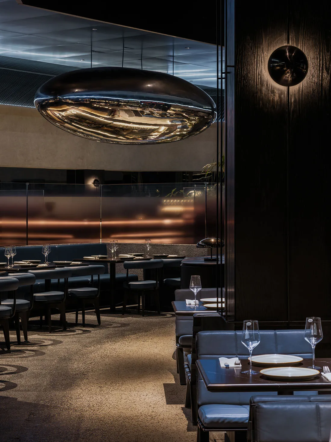 Dimly lit restaurant with black tables and chairs, wine glasses on some tables