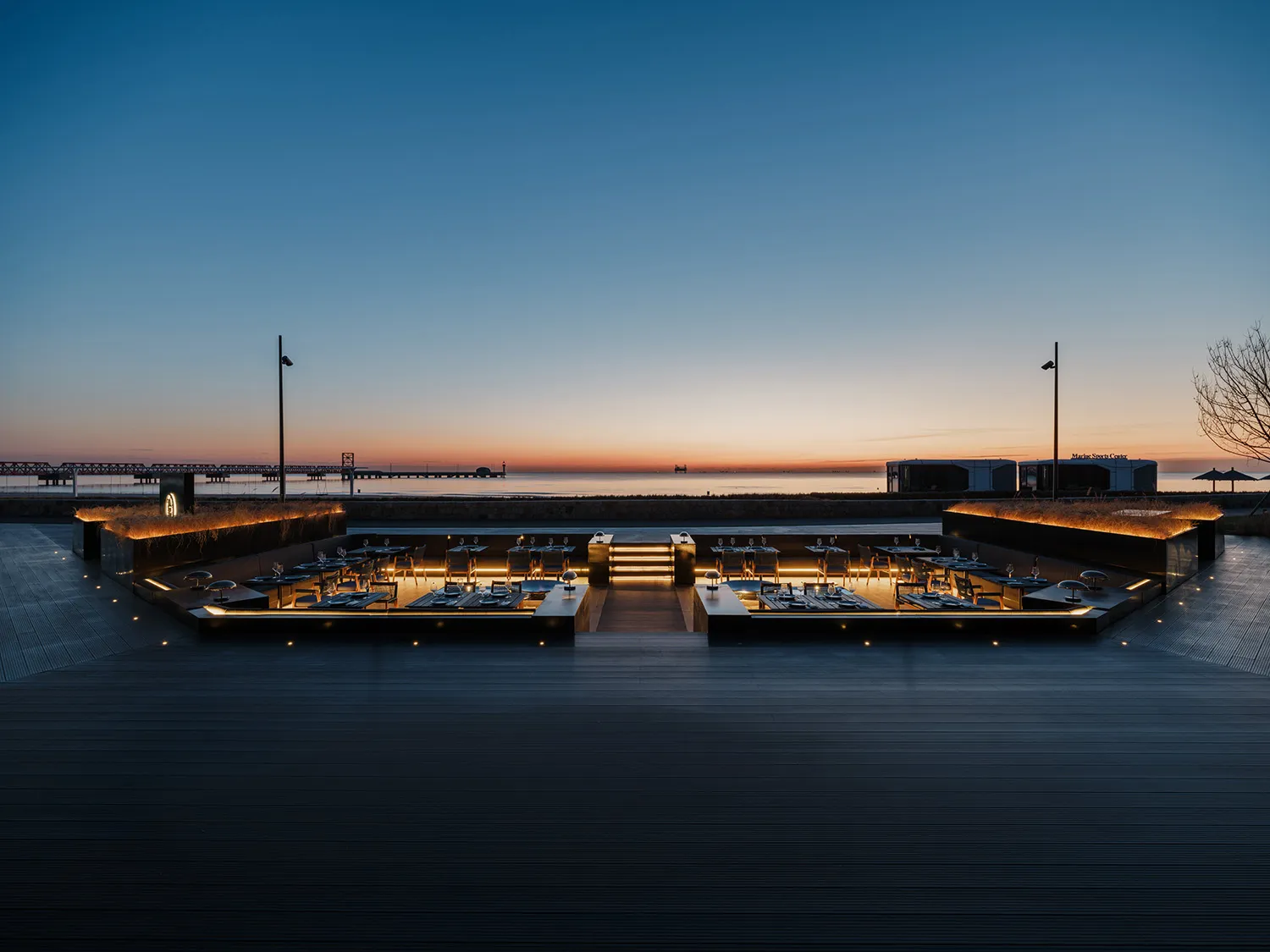 A waterfront restaurant with multiple dining tables and chairs, surrounded by a scenic view