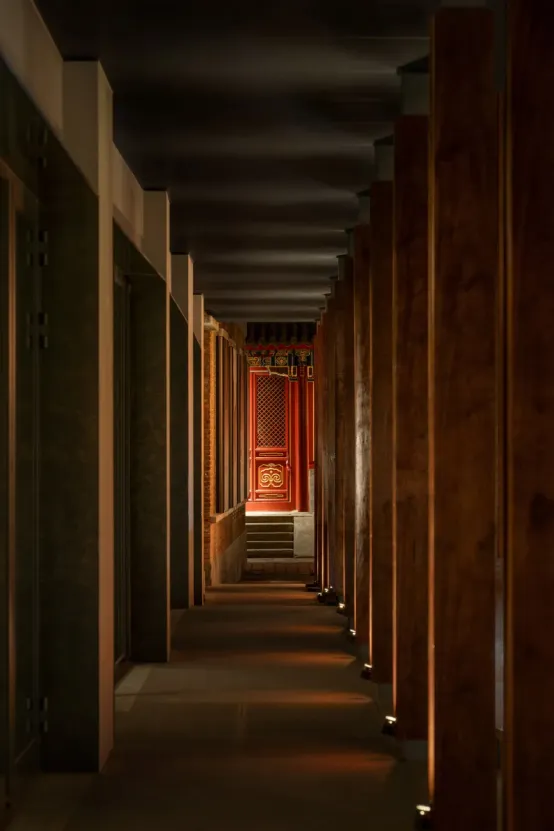 A grand ornate hallway with wooden walls and floors, featuring red-accented doors and warm lighting that enhances the beauty of the architecture