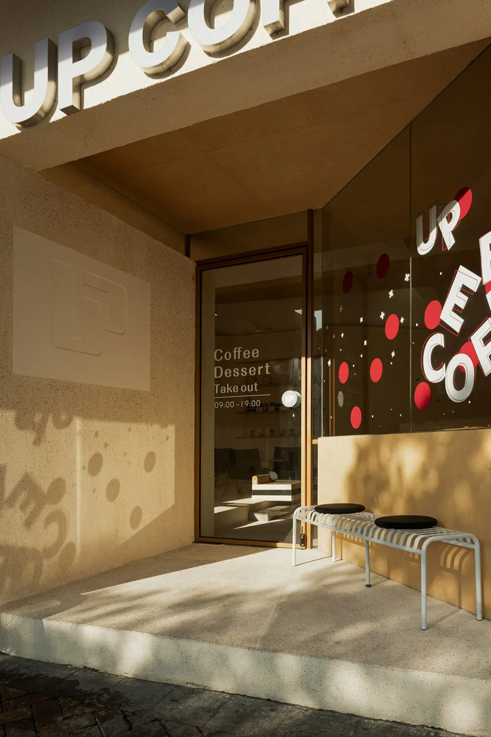 A cozy coffee shop interior with a glass door entrance, two benches, a dining table, and natural light from a window
