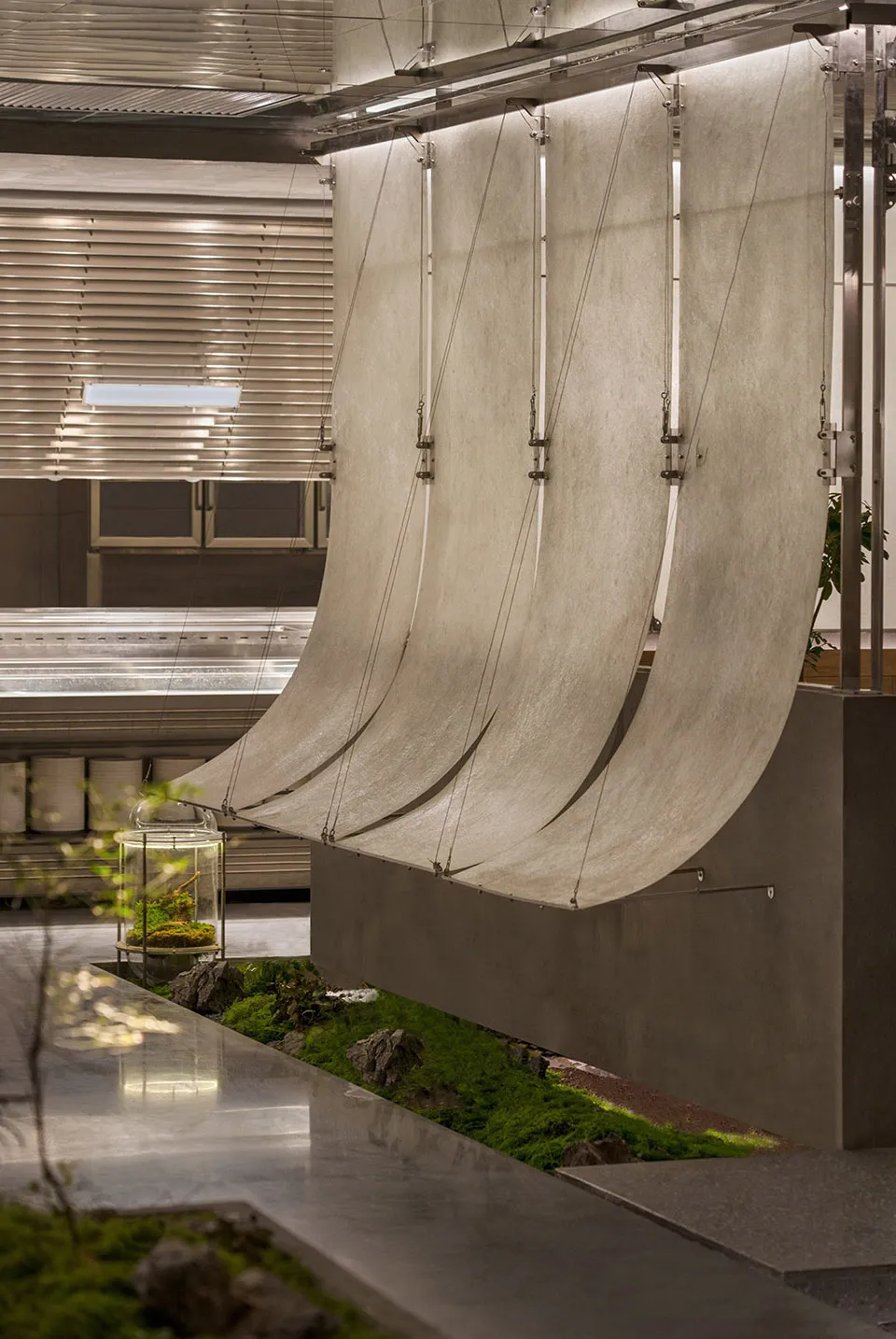 Modern industrial space with a large metal sculpture hanging from the ceiling, made of metal rods resembling a sail