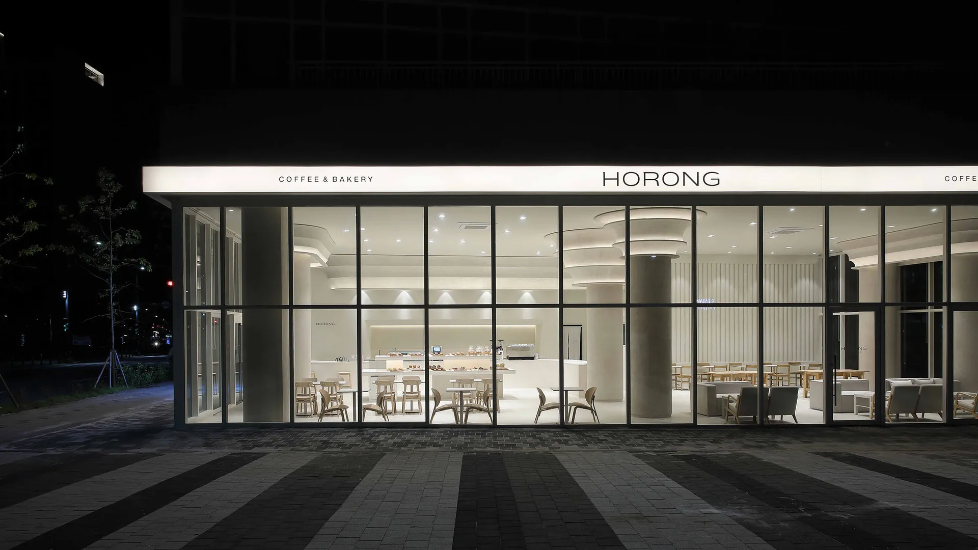 A well-lit coffee shop with tables, chairs, and a large window allowing natural light to enter