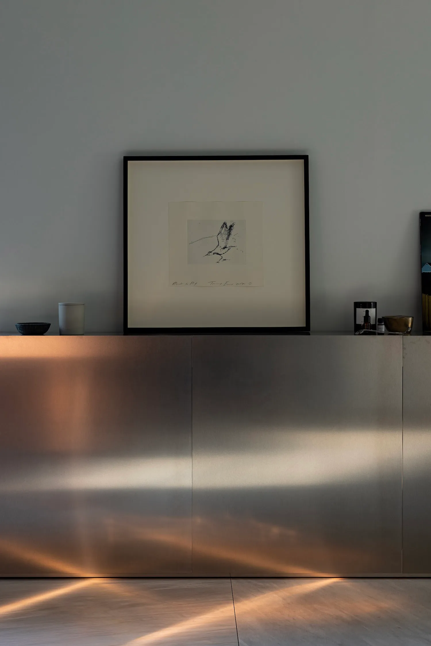 Decorative wall with a large picture and a smaller one below, accompanied by three bowls on a surface in front of it