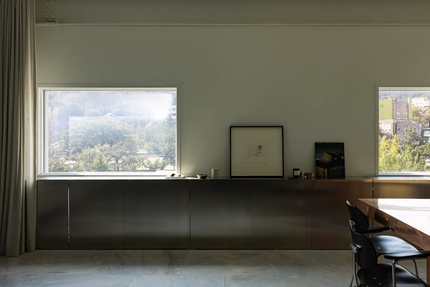 Empty living room with a large window, two chairs, a dining table, and a vase, with sunlight entering the space