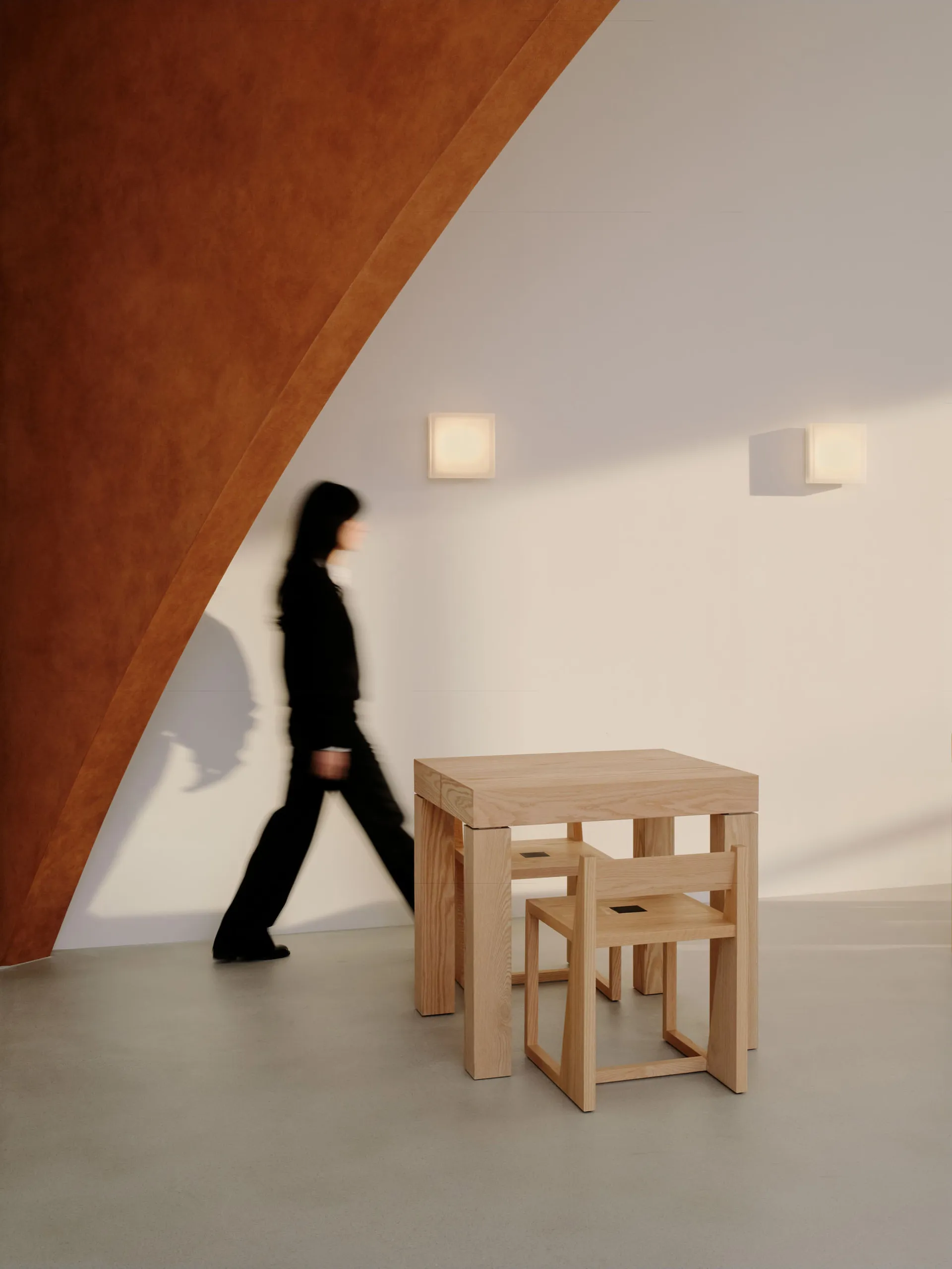 A woman walks past a wooden dining table in a casual restaurant setting with two chairs and wooden walls creating a warm atmosphere