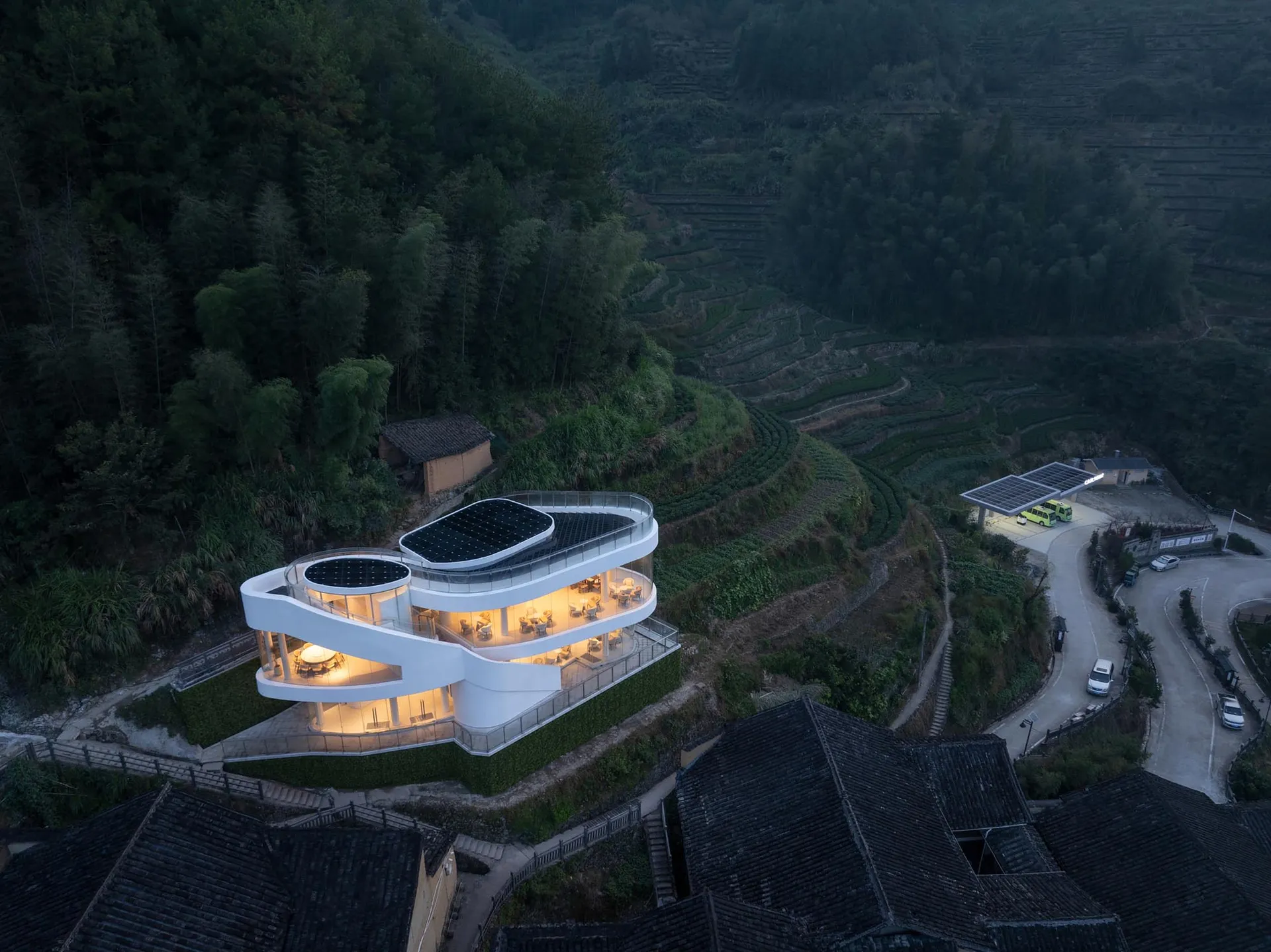 一座寧靜的現代山坡住宅照片，周圍環繞樹木與山巒，擁有大片窗戶與混凝土外牆