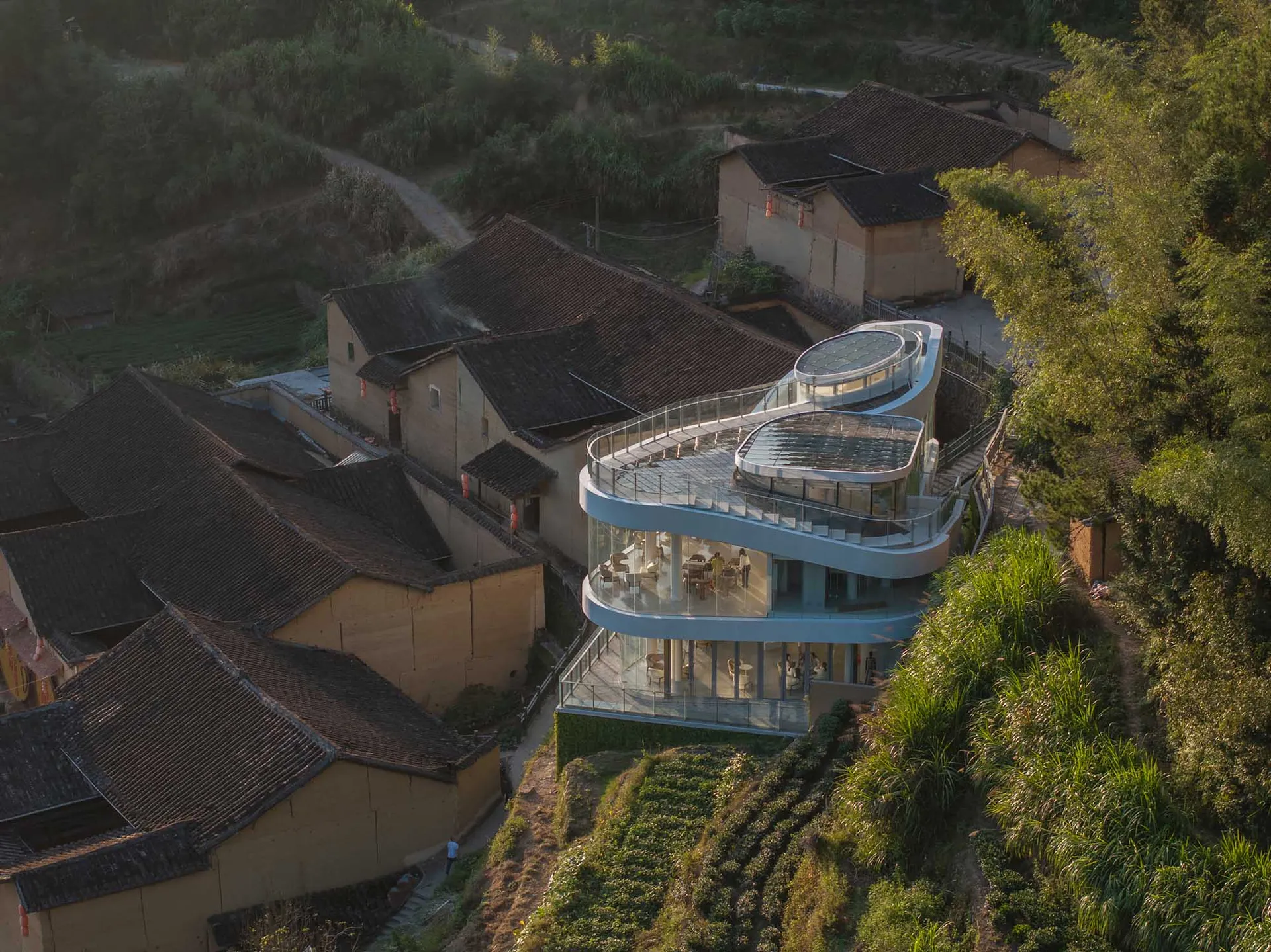 一座位於山坡上的現代住宅，擁有大型玻璃結構，融合傳統與當代建築元素