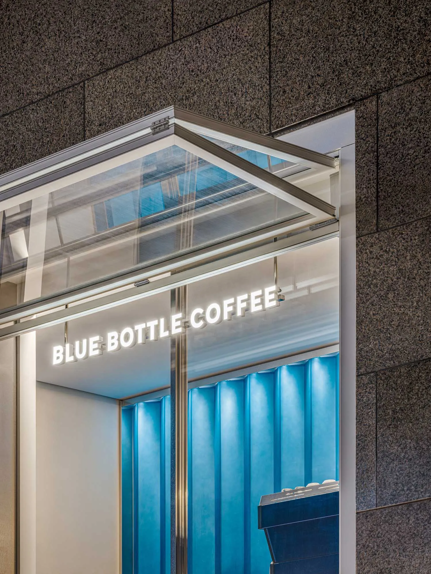 A modern coffee shop with a large window, glass, and metal elements, white and blue walls, and a clean atmosphere