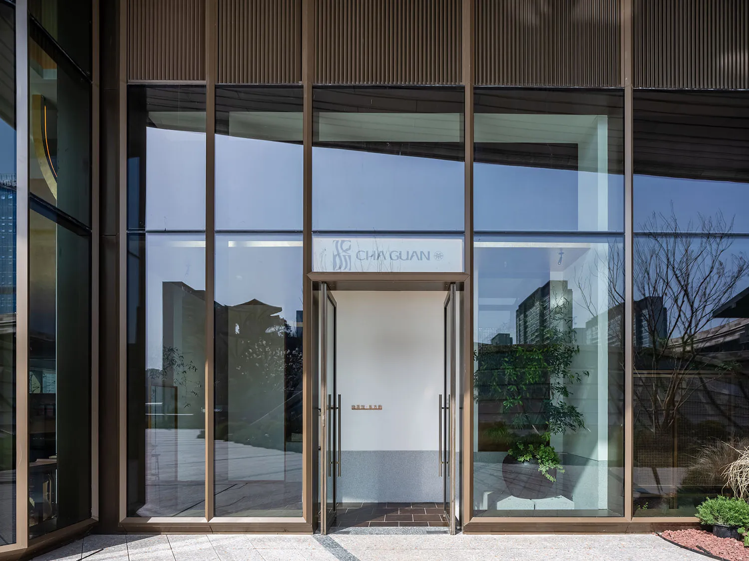 Welcoming entrance with a glass door, metal frame, and two potted plants adding a touch of greenery to the scene
