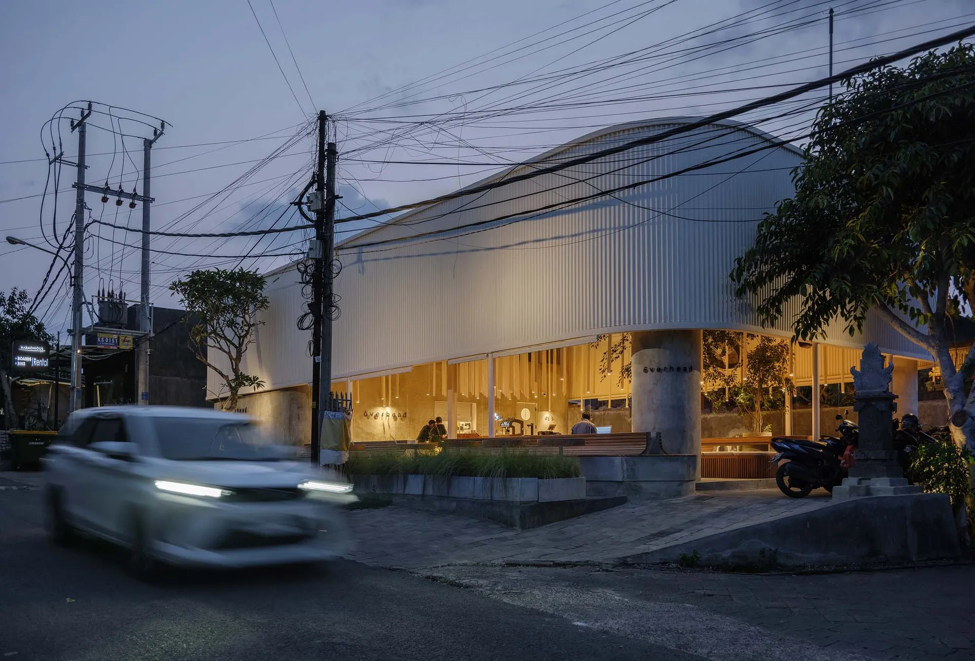 夜晚現代建築，白車行駛而過，人們在外頭走動，周圍電線環繞，充滿熱鬧氛圍