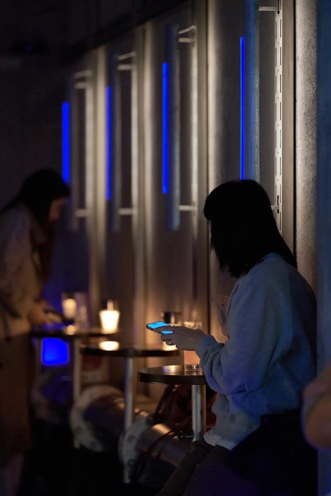 Two women sitting at a wooden bar with cups and a bottle, in a relaxed social setting
