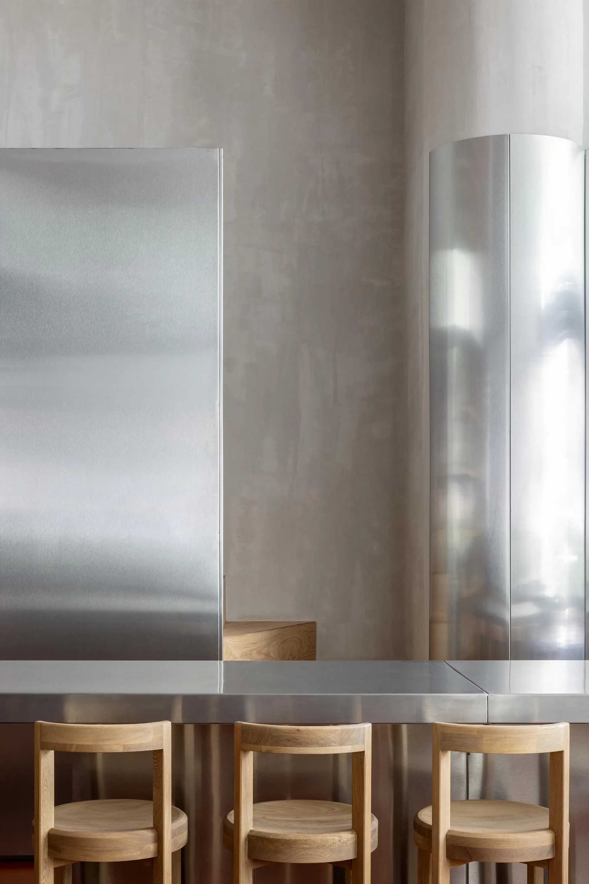 Empty dining area with a large metal table surrounded by wooden chairs in a clean and minimalistic atmosphere
