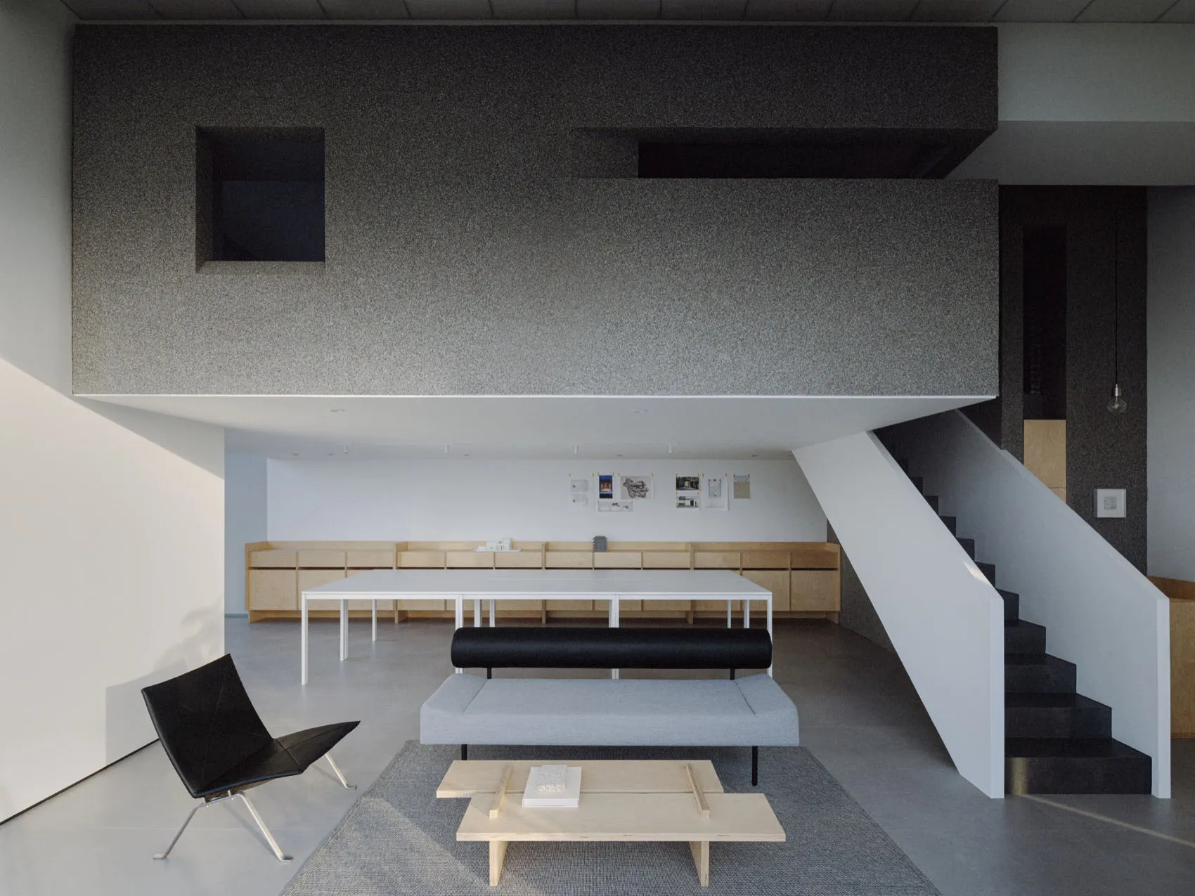 A modern living area with a large white table, black chairs, gray walls, and white surfaces, featuring two couches and a bench, creating a cozy and spacious atmosphere
