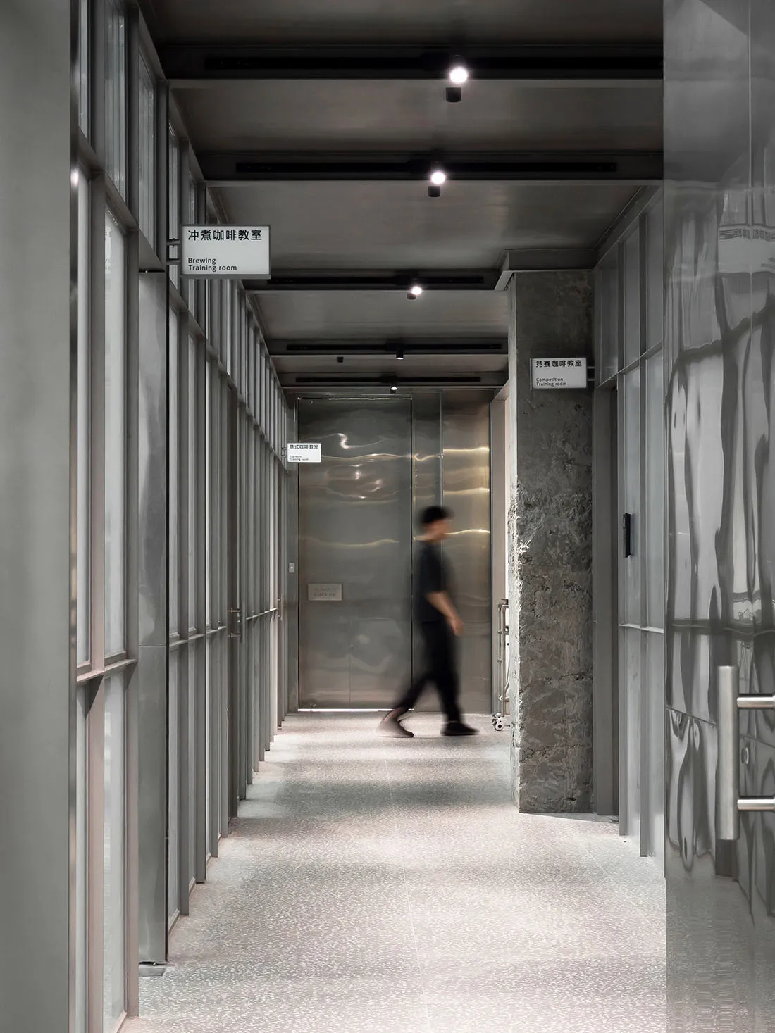 A modern hotel lobby with a silver metal finish, featuring two individuals walking down the hallway