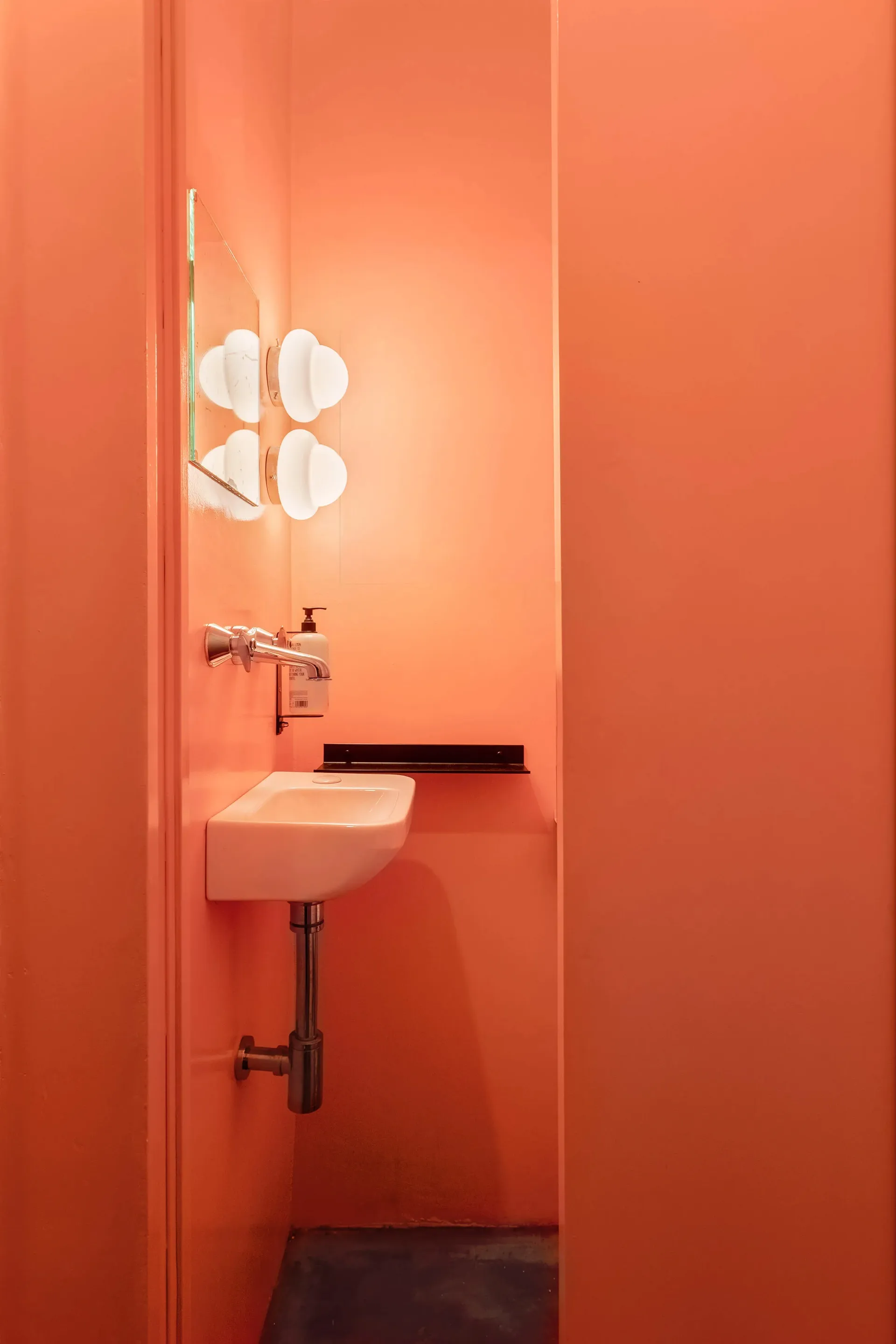 A well-lit bathroom with a wall-mounted sink, white basin, and two mirrors, painted walls in a warm hue