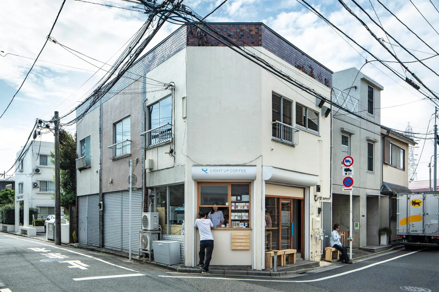 磚牆外觀的熱鬧咖啡店，白色室內設計，顧客坐在桌邊及站立店外