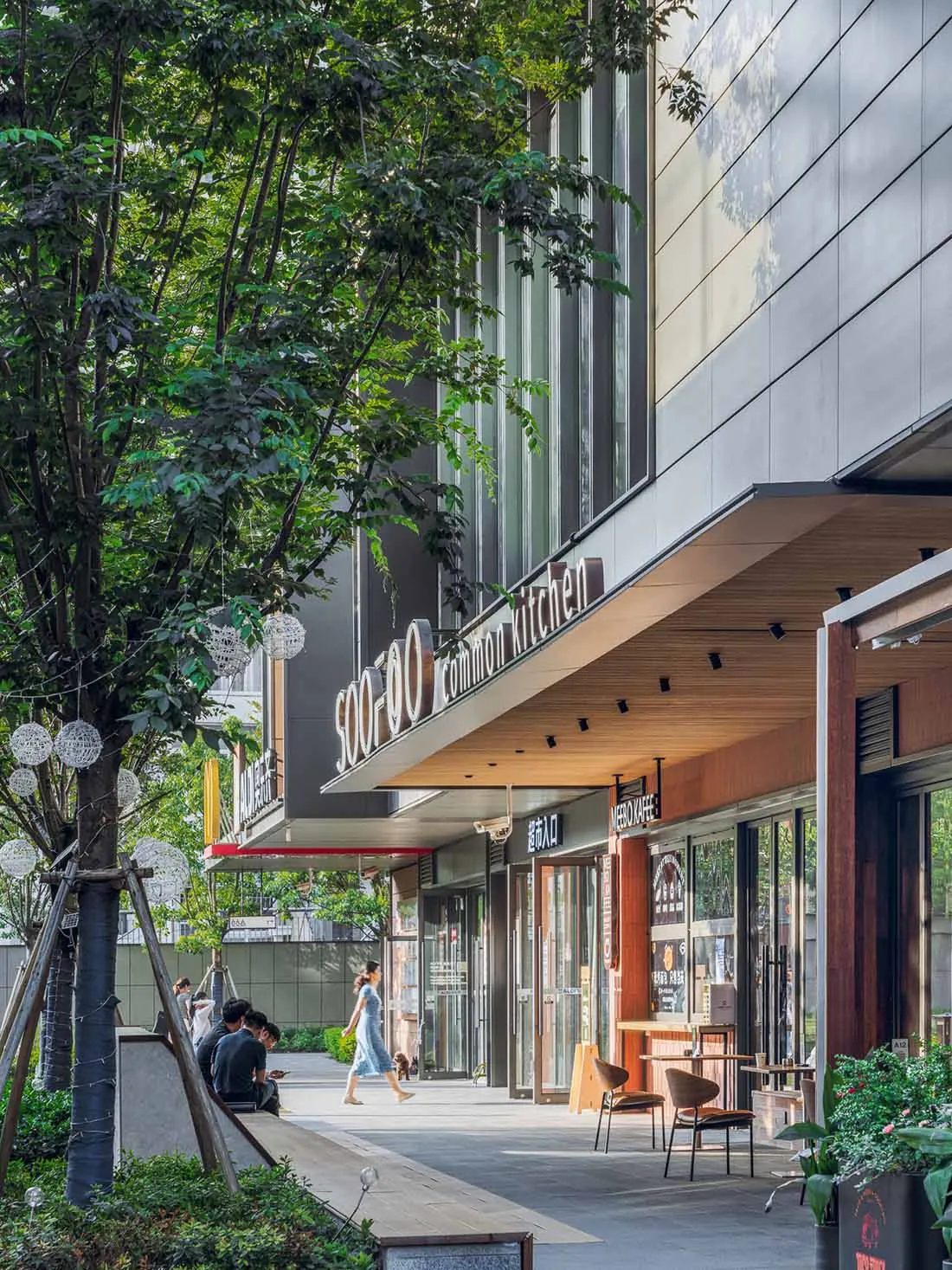 Modern restaurant with a glass front, wood accents, and natural light from a large window, set in an urban street scene with people walking by