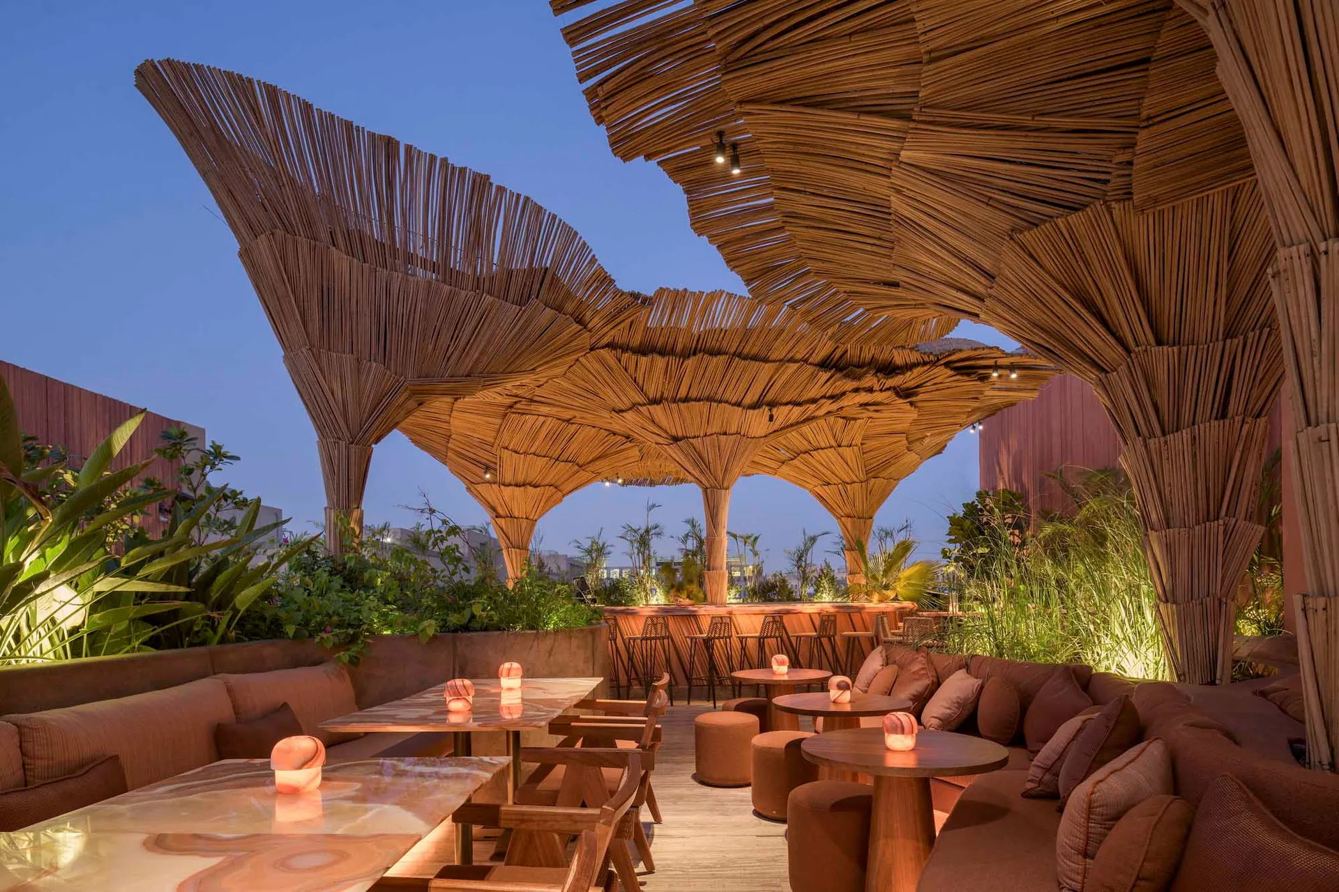 A restaurant patio with wooden structures, thatched roofs, and potted plants, creating a warm and inviting atmosphere for dining and socializing